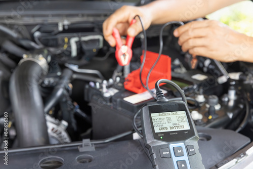 Schilderij op canvas Man is measuring AGM battery power of suv car by battery tester at home