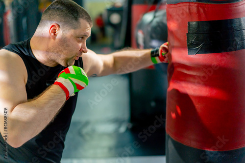 close up in a boxing fight club senior muscular trainer in a black T-shirt and with multi-colored bandages is boxing a punching bag © Guys Who Shoot