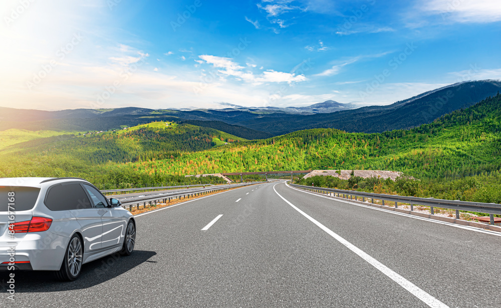 A white car drives along the highway against the backdrop of rocky mountains on a sunny day. A white car drives along the highway against the backdrop of rocky mountains on a sunny day.