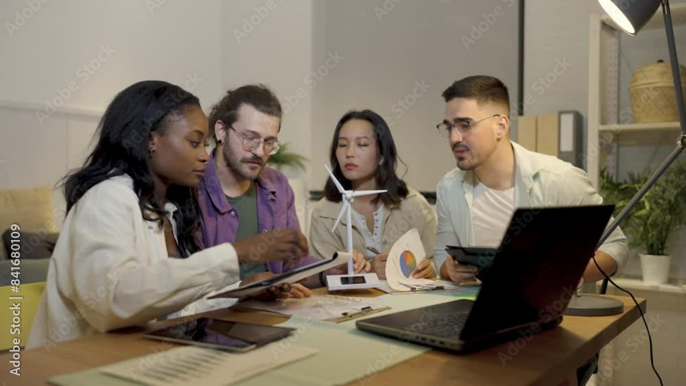 A group of four young people from diverse backgrounds gather around a model wind turbine. They share their thoughts and ideas about sustainable energy sources. A group of four young people from diverse backgrounds gather around a model wind turbine. They share their thoughts and ideas about sustainable energy sources.