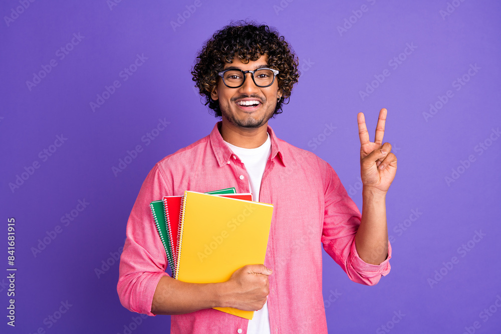 Portrait of nice young man book show v-sign wear pink shirt isolated on purple color background Portrait of nice young man book show v-sign wear pink shirt isolated on purple color background