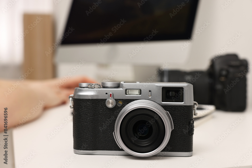 Photographer working on computer at white table with camera indoors, closeup Photographer working on computer at white table with camera indoors, closeup