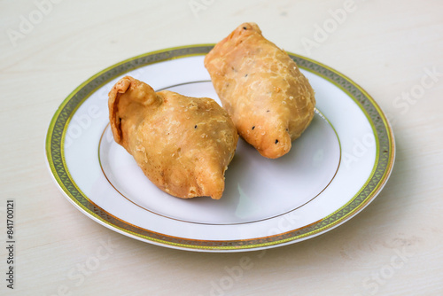 Two fried samosas on a white plate. It is also known as singara, singada, samose, somsa, sambusa, and samuza. Traditional street food from Bangladesh and the Bengal region of India. photo