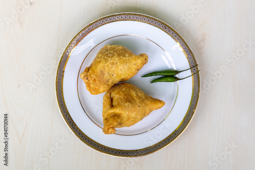 Bengali street food fried samosa or singara served on a white plate with twogreen chilies. Top view. photo