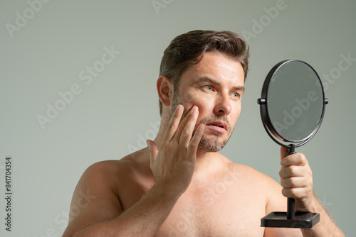 guy standing in modern bathroom at home. Male Beauty And Haircare Routine. Handsome Man Touching Hair Looking In The Mirror After Shower, Smiling To His Reflection Standing In Modern Bathroom