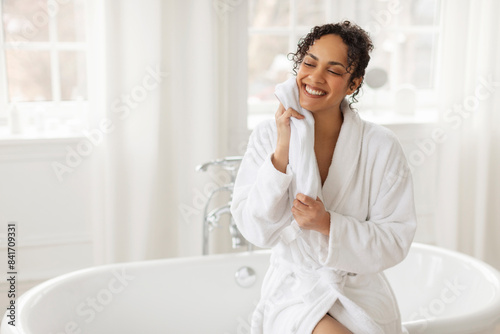 Happy African American lady drying face with towel  enjoy doing facial skincare ritual in the morning in bathroom. Woman enjoying beauty routine