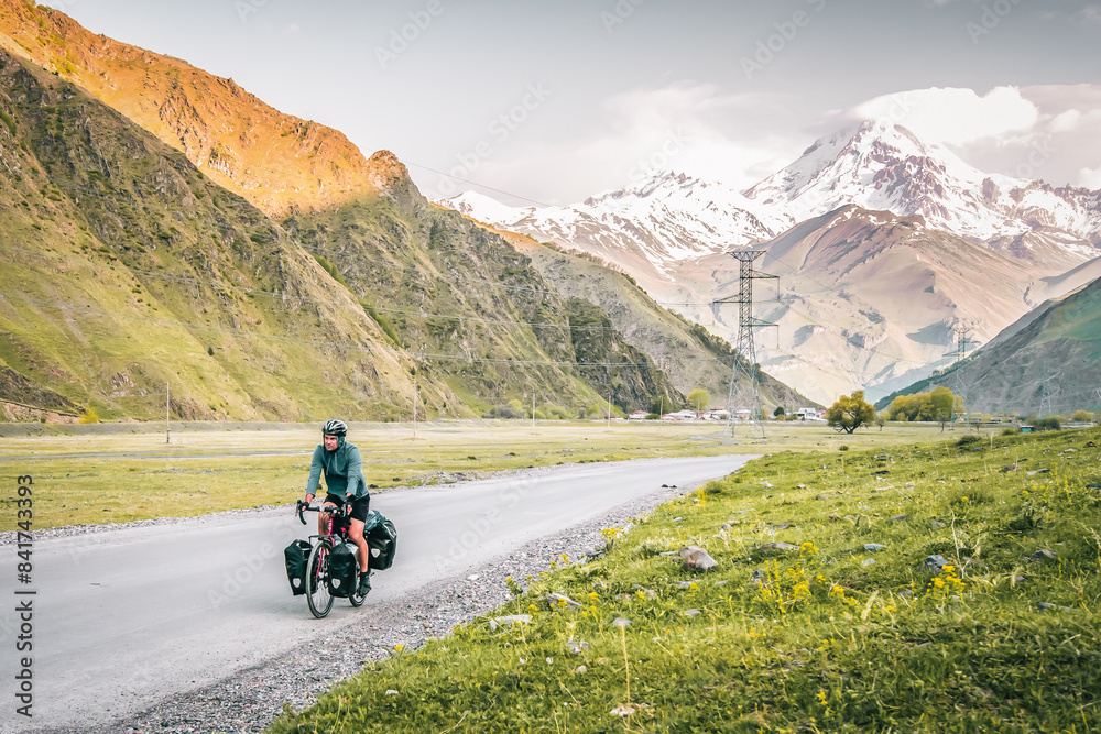 Caucasian male cyclist bicycle touring in caucasus KAzbegi mountains and Kazbek peak background. Travel around caucasus. Cycle around the world holidays outdoors Caucasian male cyclist bicycle touring in caucasus KAzbegi mountains and Kazbek peak background. Travel around caucasus. Cycle around the world holidays outdoors