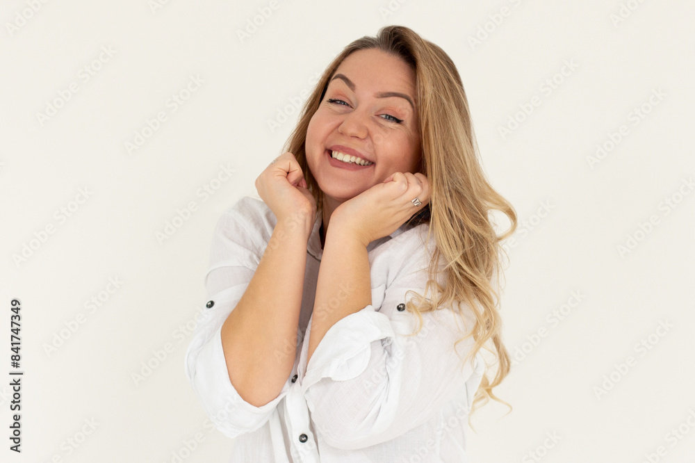 Headshot of pleased high spirit pretty female model, has warm pleasant smile, keeps hands under chin, wears white shirt, isolated over white background. Happiness concept Headshot of pleased high spirit pretty female model, has warm pleasant smile, keeps hands under chin, wears white shirt, isolated over white background. Happiness concept