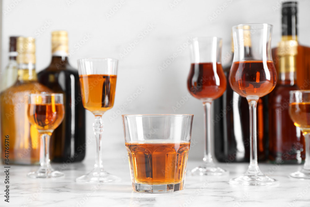 Delicious liqueurs in glasses and bottles on white marble table Delicious liqueurs in glasses and bottles on white marble table