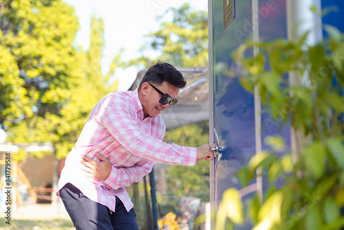 Tableau sur toile A man in distress desperately tries to open a locked portable toilet in a park setting, reflecting urgency and discomfort