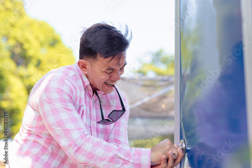 A man in distress desperately tries to open a locked Portapotty in a park setting, reflecting urgency and discomfort. Sudden diarrhea concept. photo