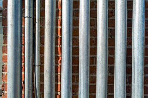 Detail of metal conduits running up and down in parallel along an exterior brick wall photo