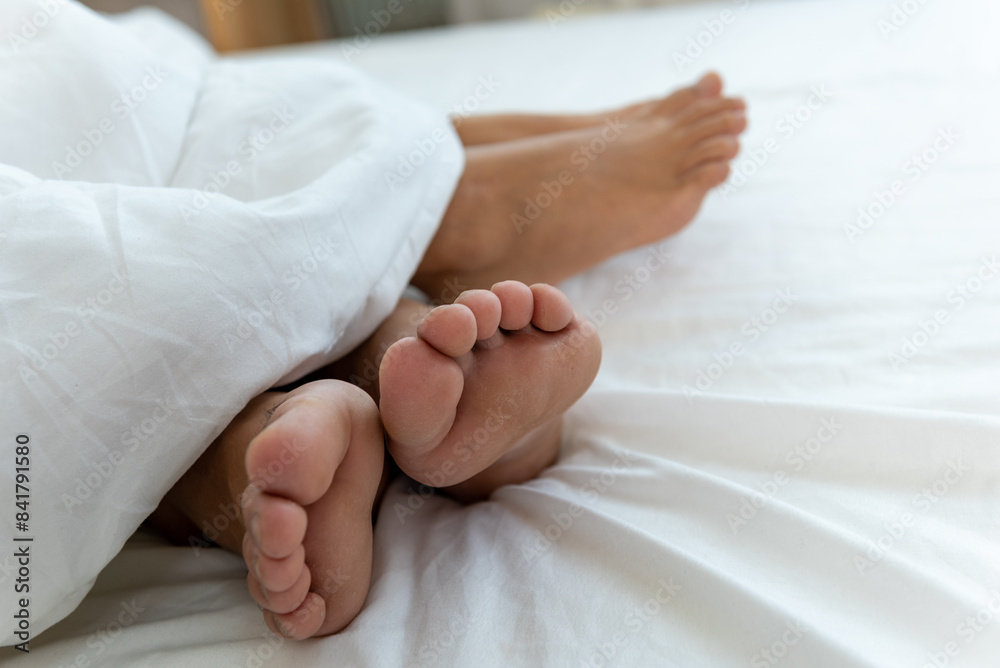 A couple's feet stick out from under a white blanket. A couple's feet stick out from under a white blanket.