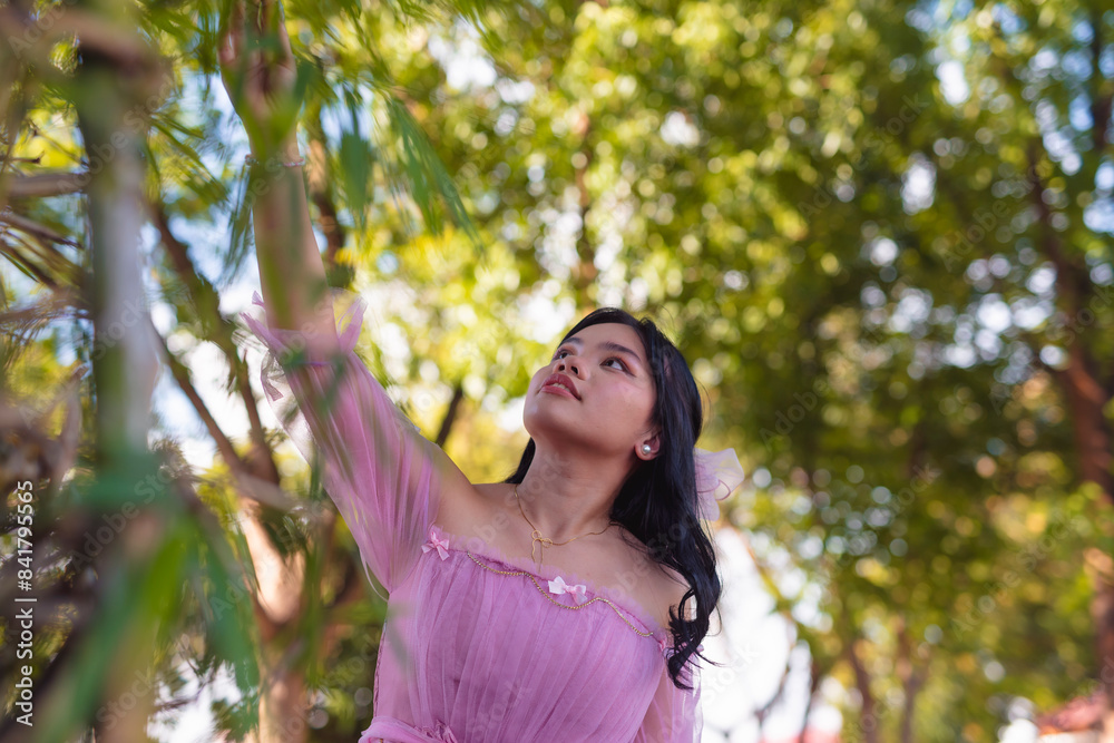 Young woman in pink dress reaching up in park setting