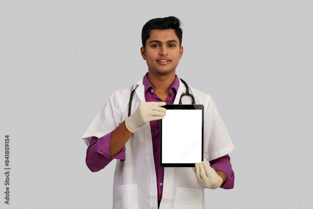 young handsome Indian male doctor with stethoscope on his neck, wearing gloves showing tablet with empty screen isolated on white background young handsome Indian male doctor with stethoscope on his neck, wearing gloves showing tablet with empty screen isolated on white background