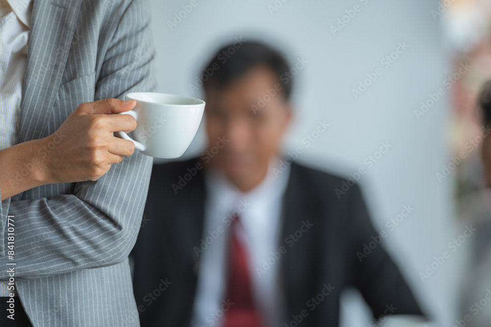 A business woman holding a coffee cup with a man in the background A business woman holding a coffee cup with a man in the background