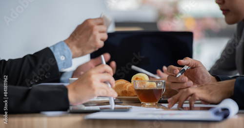 A group of people are having a meeting in an office. They are discussing some documents and drinking tea.