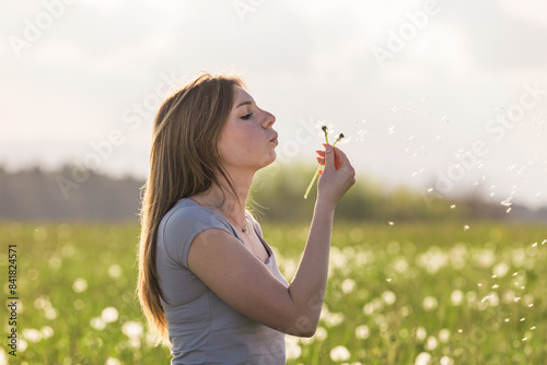 Young woman blowing dandelions  on the green meadow with the summer sun in the background. Dream  and life optimism concepts.