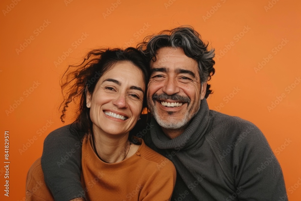 Portrait of a joyful latino couple in their 30s showing off a thermal merino wool top in pastel orange background