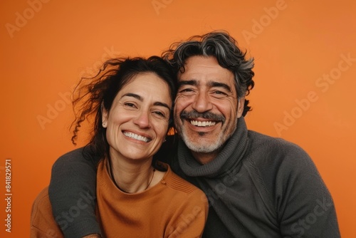 Portrait of a joyful latino couple in their 30s showing off a thermal merino wool top in pastel orange background © Markus Schröder