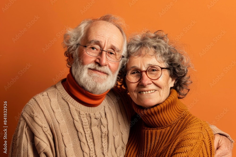 Portrait of a merry couple in their 70s wearing a classic turtleneck sweater in pastel orange background Portrait of a merry couple in their 70s wearing a classic turtleneck sweater in pastel orange background