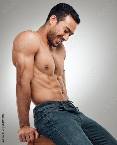 Man, chair and topless in studio for fitness, wellness and strong abs muscle on gray background. Male person, denim jeans and shirtless for health, bodybuilder and proud of body or workout results