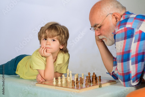 Chess competition. Little boy thinking about next move in game of chess. Board games. Grandfather and grandson playing chess. Child boy play chess with grandpa. Brain development and logic concept.