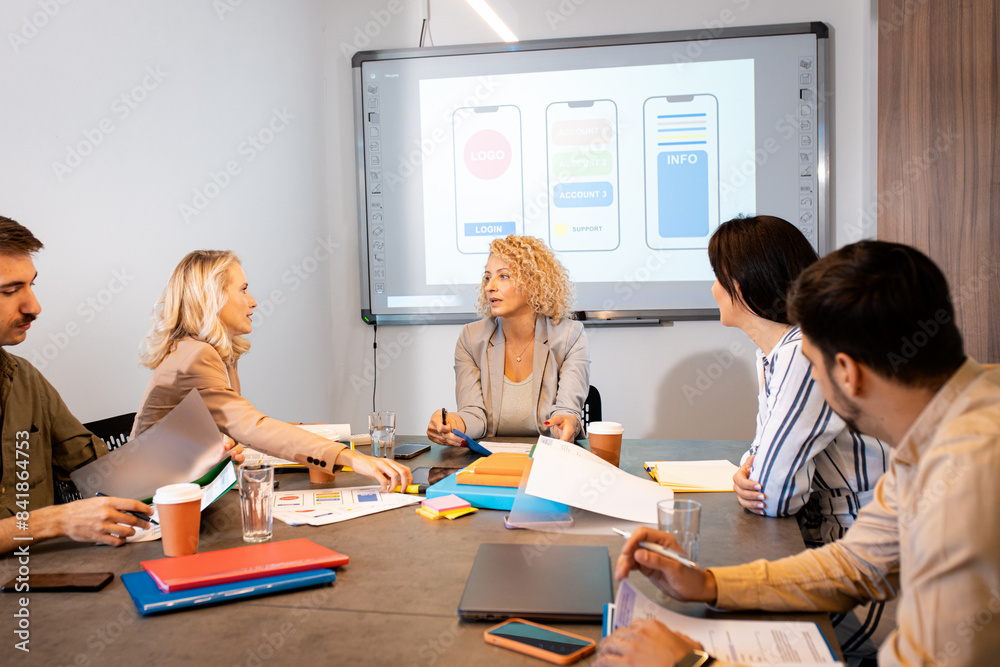 Group of business people sitting in a meeting room discussing a design for a smartphone application. Group of business people sitting in a meeting room discussing a design for a smartphone application.