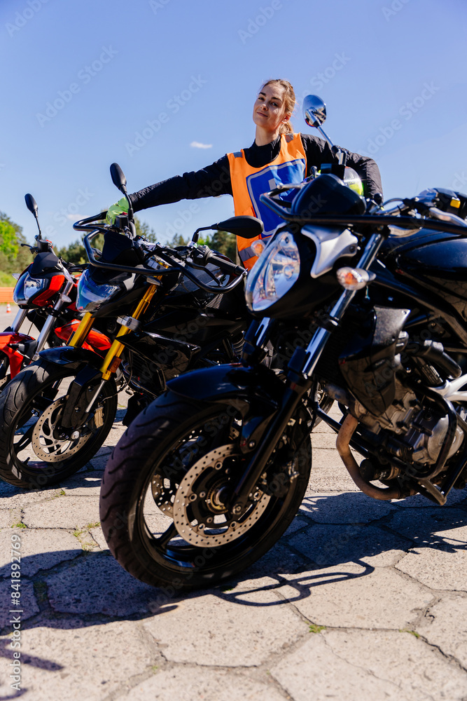 A woman in an orange vest stands next to a row of motorcycles A woman in an orange vest stands next to a row of motorcycles
