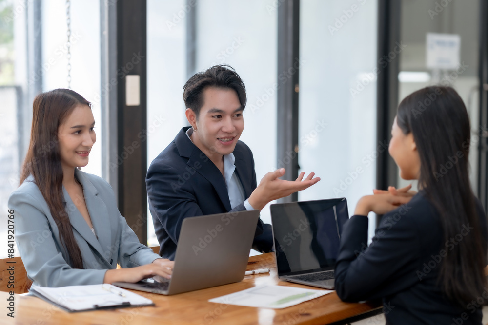 Three business professionals engaged in a meeting, discussing ideas and using laptops, in a bright, modern office setting. Three business professionals engaged in a meeting, discussing ideas and using laptops, in a bright, modern office setting.