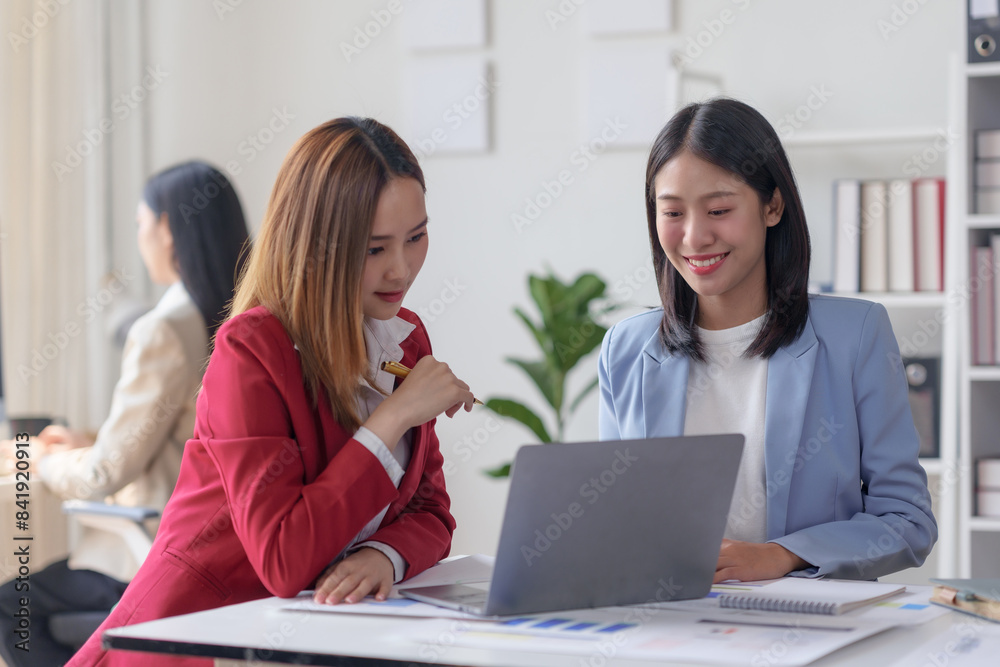 Two businesswomen collaborate on a project using a laptop in a modern office environment. Teamwork, productivity, and professional discussion. Two businesswomen collaborate on a project using a laptop in a modern office environment. Teamwork, productivity, and professional discussion.