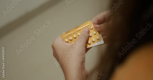 Close up of a hands young woman holding a package of birth control pills. She takes out one pill and takes it. Contraceptives and birth control. Childfree people.