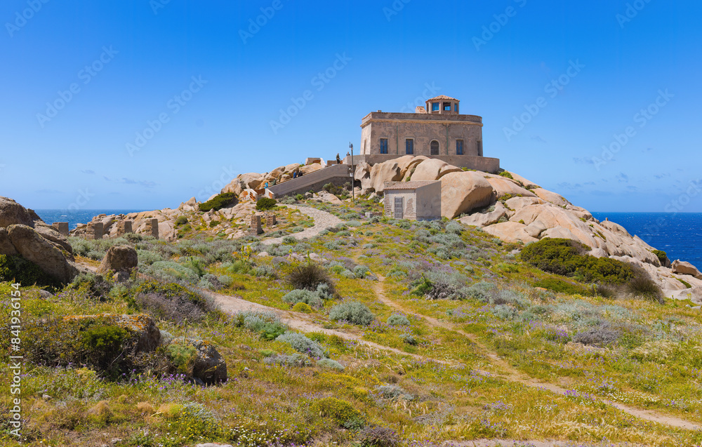 Faro del Cabo Testa en Cerdeña, Italia, durante la primavera. La estructura de piedra se asienta sobre formaciones rocosas en un paisaje costero salpicado de vegetación baja y flores silvestres. Faro del Cabo Testa en Cerdeña, Italia, durante la primavera. La estructura de piedra se asienta sobre formaciones rocosas en un paisaje costero salpicado de vegetación baja y flores silvestres.
