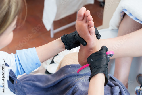 young Asian spa professional using foot file on elderly customer's foot during spa treatment. Emphasis on hygienic and detailed foot care service in a serene spa setting, ensuring relaxation.