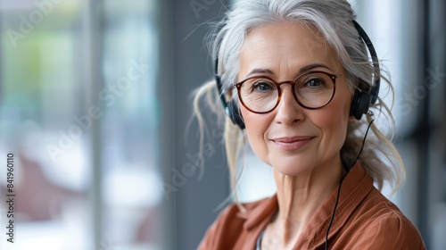 Porträt einer fröhlich lächelnden reifen Frau mit grauen Haaren und Brille, die ein Headset trägt, modernes Büro. Call-Center, professionelle Unterstützung, Online-Ausbildung für ältere Menschen