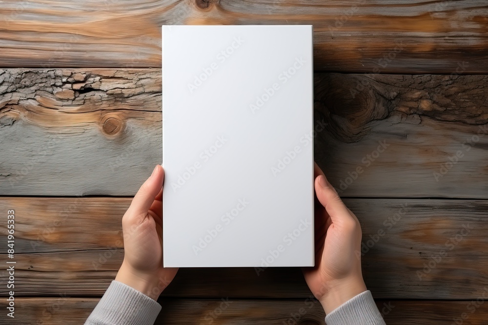 A man holds a sheet of A4 format in his hands on a wooden background.