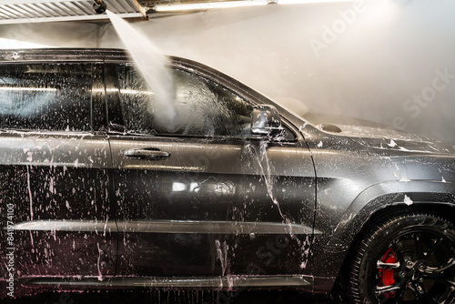 Washing the foam from the surface of the vehicle. Cleaning the car body with a high pressure water jet at a self serve car wash. photo