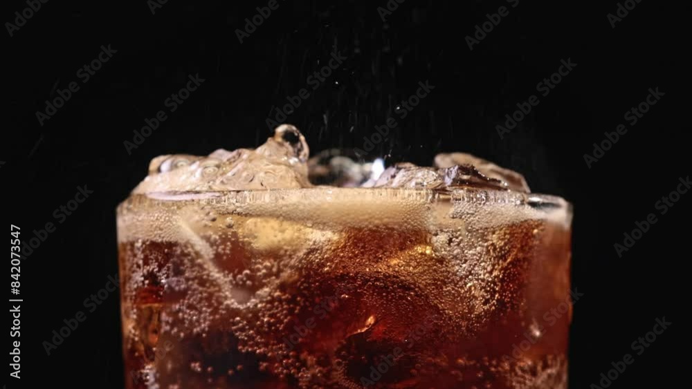 Closeup of pouring cola drink with ice cubes. Fizzing cola with ice in glass. Refreshing tasty cola drink.