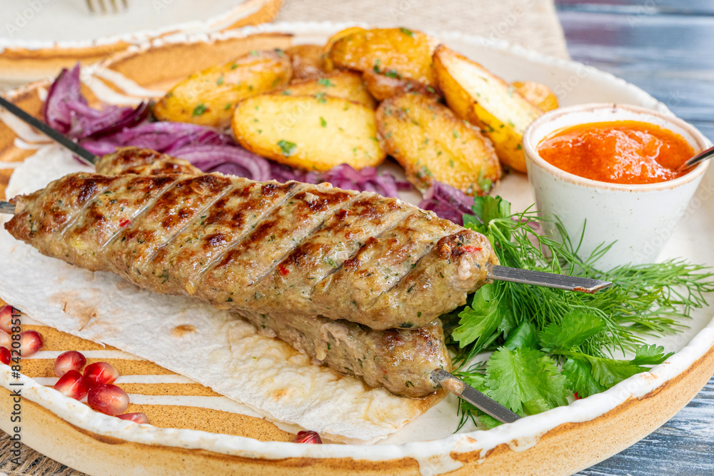 Georgian lula kebab with baked potatoes, sauce and greens. Grilled souvlaki, minced meat kebap, lamb on skewers Georgian lula kebab with baked potatoes, sauce and greens. Grilled souvlaki, minced meat kebap, lamb on skewers
