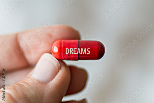 Person holds with his fingers red tablet with the inscription "Dreams". Close-up photo. Medicine addiction concept 