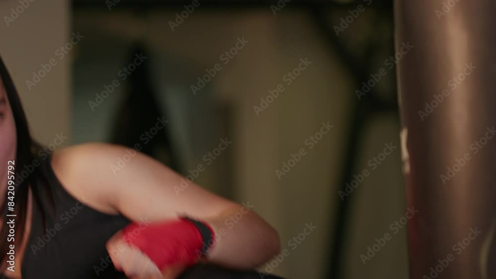 Closeup young pretty female boxer training hard hitting the punching bag in a gym, overcoming willpower, energy and skill as a professional fighter, sportswear Closeup young pretty female boxer training hard hitting the punching bag in a gym, overcoming willpower, energy and skill as a professional fighter, sportswear