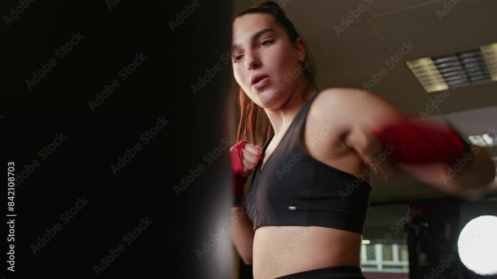 Closeup young pretty female boxer training hard hitting the punching bag in a gym, overcoming willpower, energy and skill as a professional fighter, sportswear Closeup young pretty female boxer training hard hitting the punching bag in a gym, overcoming willpower, energy and skill as a professional fighter, sportswear