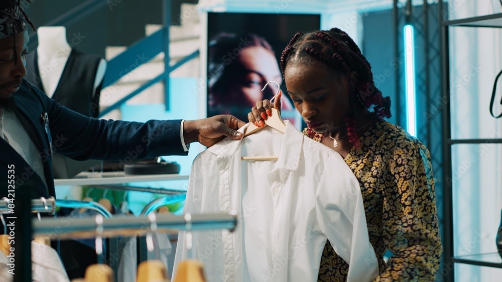 Obraz premium African american shopper looking for pregnancy clothing items, shopping session at department store. Employee offering suggestions for pregnant client, trendy designer brands. Camera A.