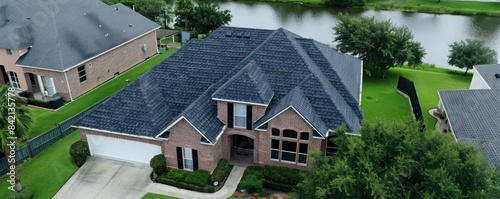 An aerial view of a residential roof with significant damage. Tiles are missing and broken, revealing underlying structures. The roof shows signs of wear and tear, set against a backdrop of lush trees photo