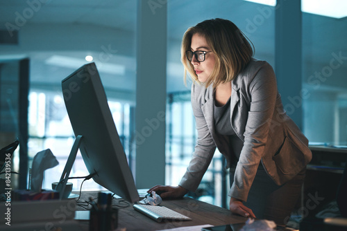 Woman, employee and reading on computer in office on browsing internet, online and research for ideas. Female person, workplace and desk with deadline or overtime, project and standing as hr photo