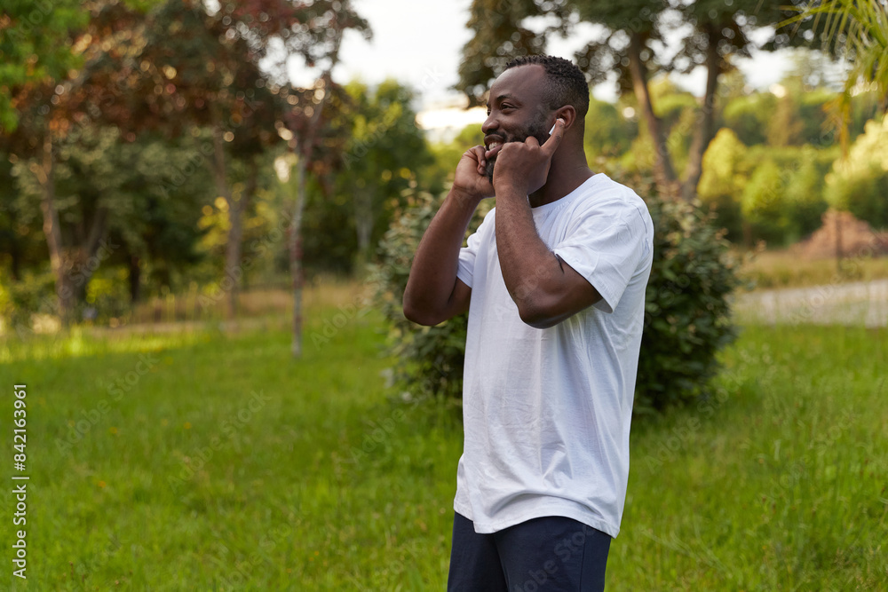 Happy young adult african american man enjoying music and dancing in the park wearing headphones Happy young adult african american man enjoying music and dancing in the park wearing headphones
