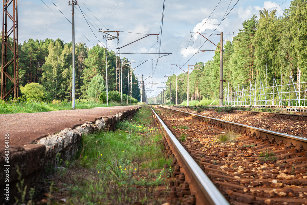 Panorama of a typical eastern european russian style railway infrastructure: an electrified railway line in a latvian forest in Pabazi train station with a train station platform at sunset in Latvia. Panorama of a typical eastern european russian style railway infrastructure: an electrified railway line in a latvian forest in Pabazi train station with a train station platform at sunset in Latvia.