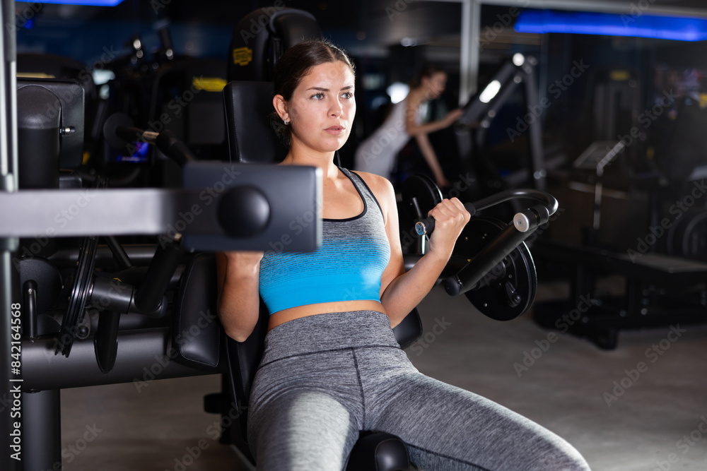 Fototapeta premium Girl does exercises to strengthen muscles of arms and shoulders, increase muscle volume and contouring. Athletics, self-study in fitness center