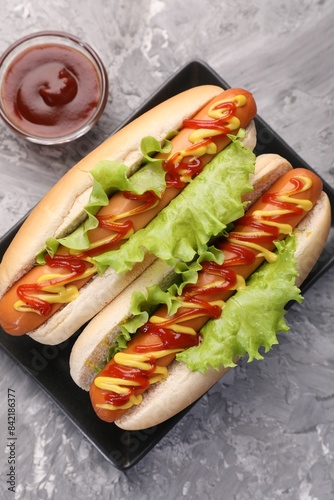 Photography Tasty hot dogs with lettuce, ketchup and mustard on grey textured table, flat la