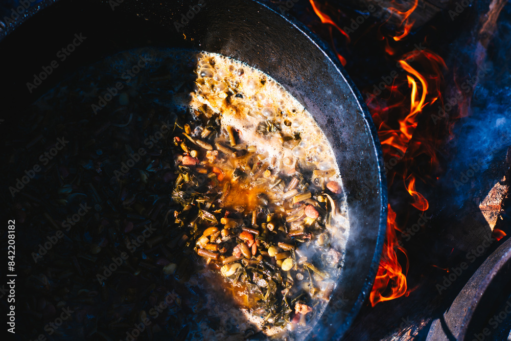 © Andrew Kornylak - A cast iron pot full of stewed vegetables over an open fire, half-lit by sunlight